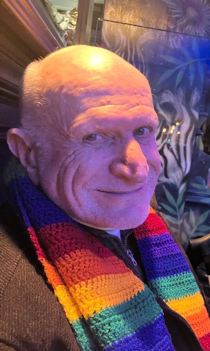 An older man in a rainbow scarf, smiling at the camera